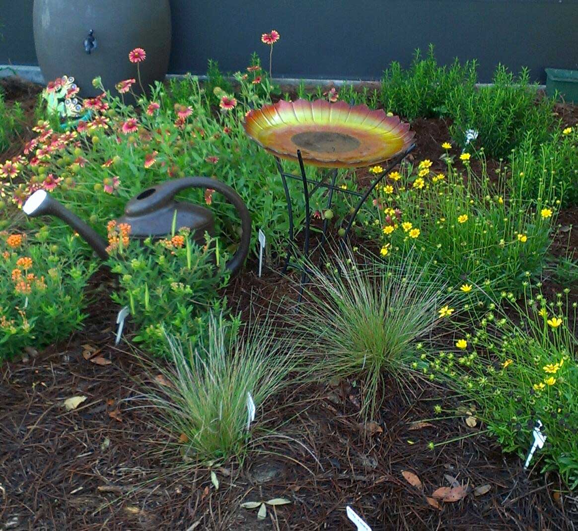 bird bath, rain barrel, watering can, yellow and red flowers