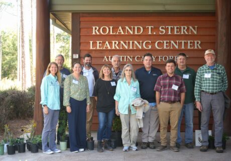 Twelve people stand in front of the Roland T. Stern Learning Center, with plants in pots on the ground near them.